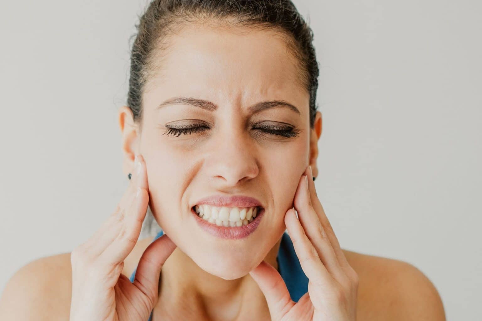 Woman pressing both sides of her jaw with a painful expression.