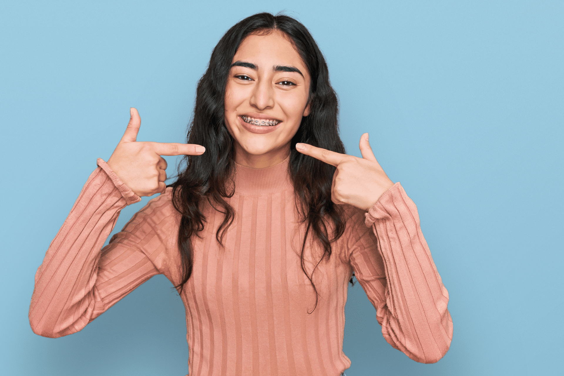 Teen girl smiling and pointing to her braces against a blue background